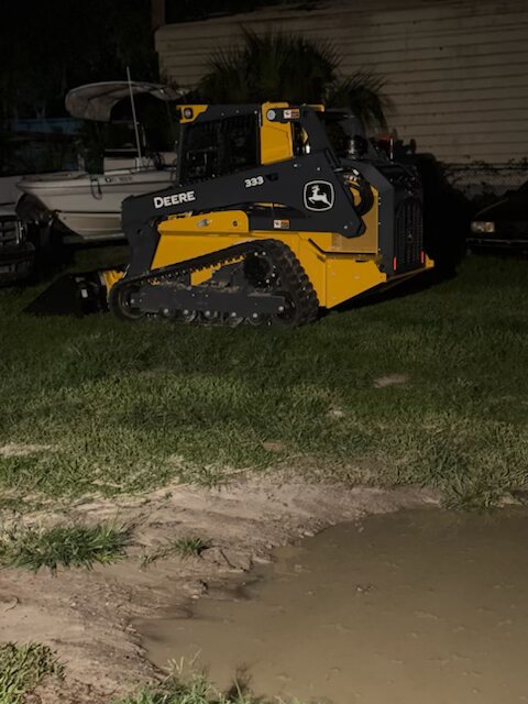 Deere excavator secured on a flatbed trailer at sunset with cleared land in the background
